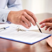 Young woman is signing financial contract with male realtor. Close-up.